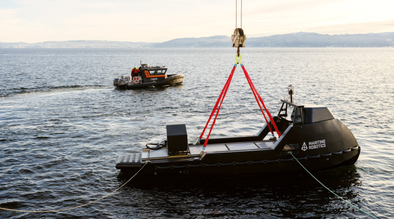 Mariner X vessel being lowered into the water using a crane system, supported by a crewed boat.