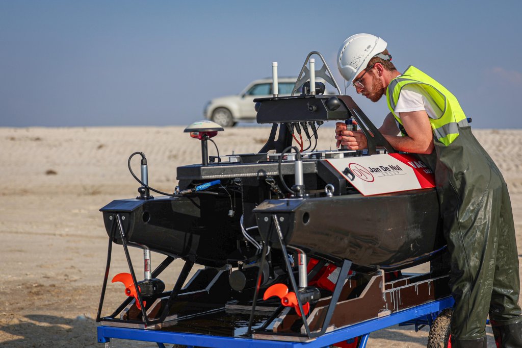 A person in a white helmet  and safety vest working on a USV vessel.
