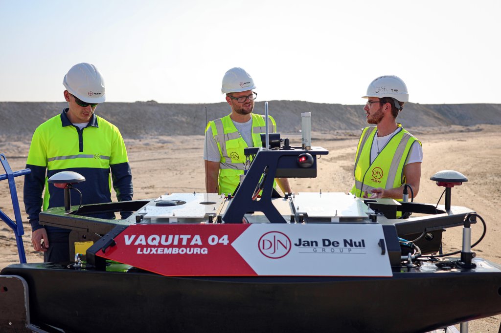 A group of men wearing safety vests and helmets. An Otter USV stands in front of them.